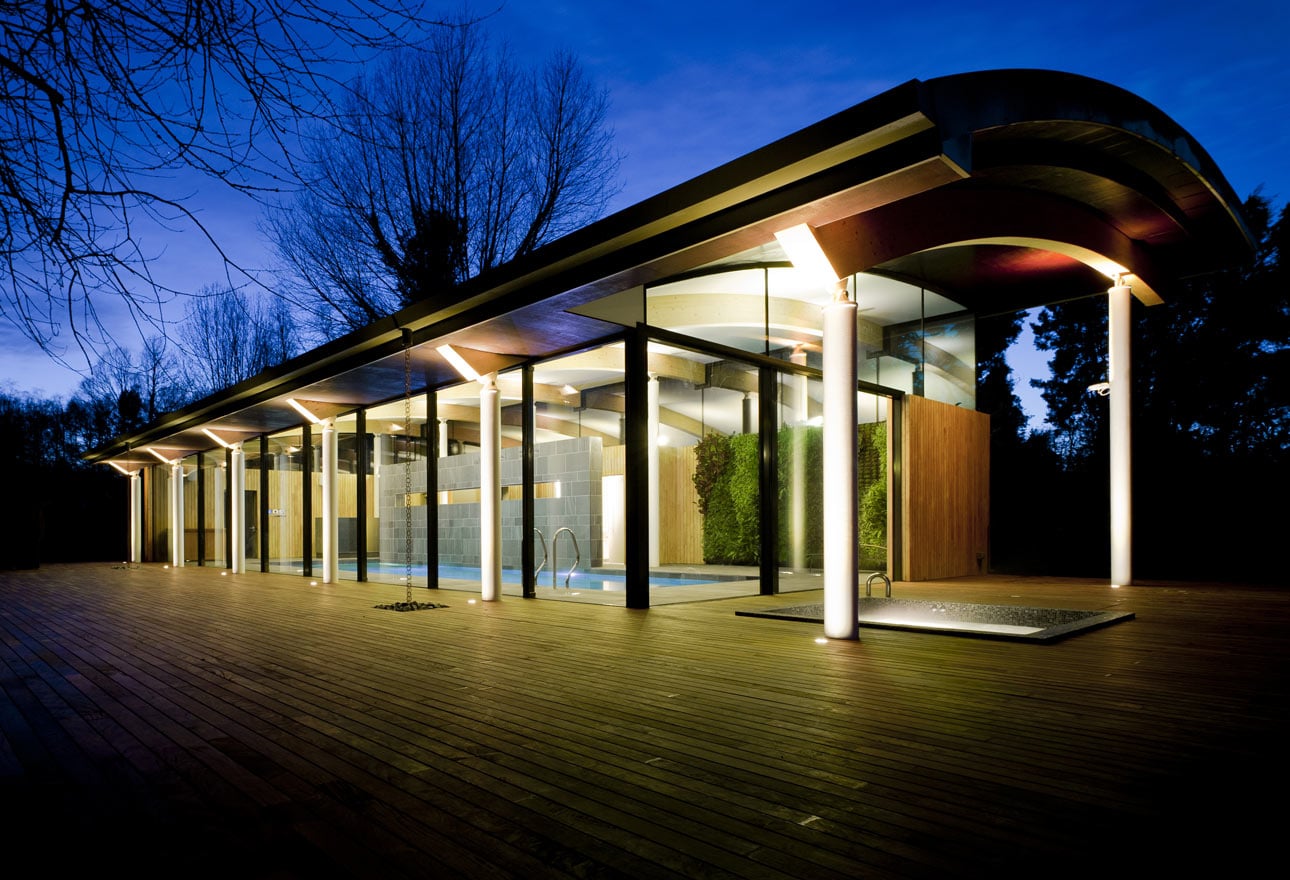 Nighttime view of contemporary hardwood decking wrapping pool house